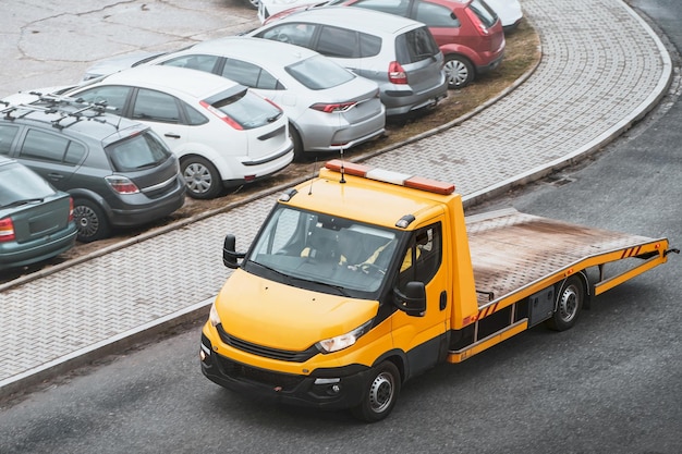 Photo une voiture en panne dans une rue urbaine attend une dépanneuse orange pour la sauver. la dépanneure a un plateau et un treuil à l'avant.