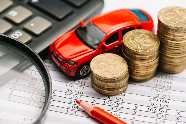 Voiture; pile de pièces de monnaie; crayon de couleur; calculatrice et loupe sur le rapport financier