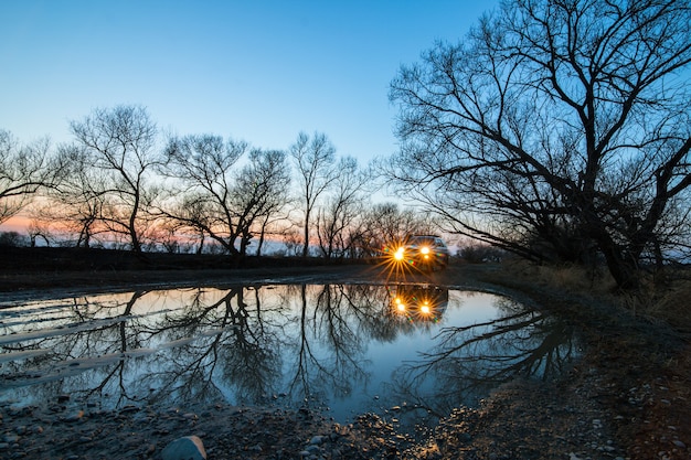 Une voiture près d'une flaque d'eau le soir avec les phares allumés