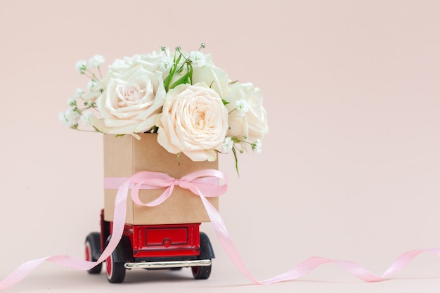 Voiture rouge avec une boîte-cadeau de fleurs roses sur le toit sur fond rose. Joyeuse Saint-Valentin, fête des mères, 8 mars, concept de carte de vacances Journée mondiale de la femme, livraison de fleurs.