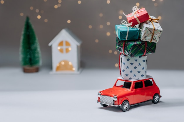 Voiture rouge avec des cadeaux sur le toit. Dans le contexte de la maison et de l'arbre. Concept sur le thème de Noël et du nouvel an.