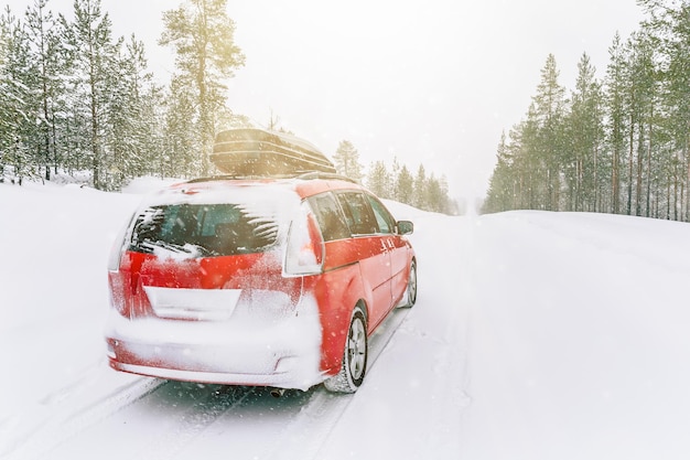 Voiture rouge avec coffre de toit sur la route de neige d'hiverxASnow forêt d'hiver avec voiture rouge sur la route