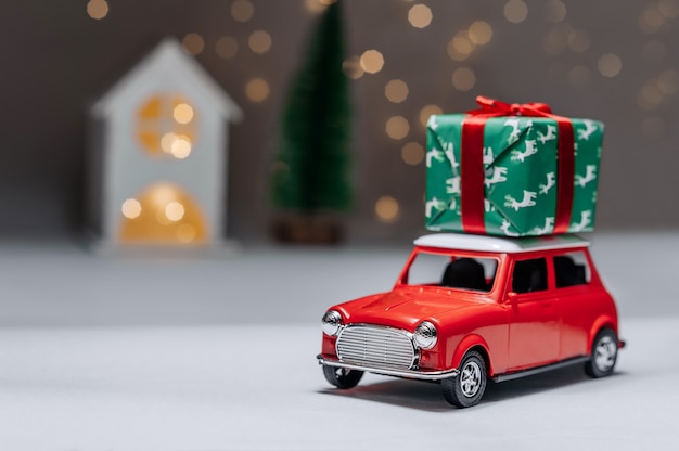 Une voiture rouge sur fond de forêt et une maison apporteront des cadeaux de Noël.