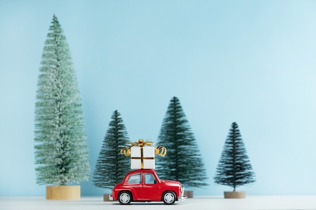 Voiture rouge de Noël avec une boîte-cadeau dans une forêt de pins. Carte de bonne année