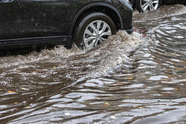 La voiture roule dans une flaque d'eau sous une pluie battante Éclaboussures d'eau sous les roues d'une voiture Inondations et hautes eaux dans la ville