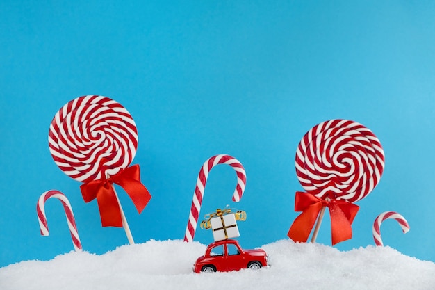 Voiture de Santa rouge avec cadeau sur le toit dans la forêt d'arbres de Noël avec des bonbons et des bonbons sucettes