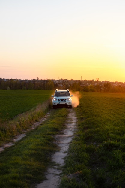 Voiture suv blanche sur la route du champ au coucher du soleil