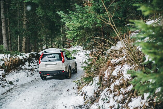 Voiture suv avec chaîne sur roues dans la forêt enneigée