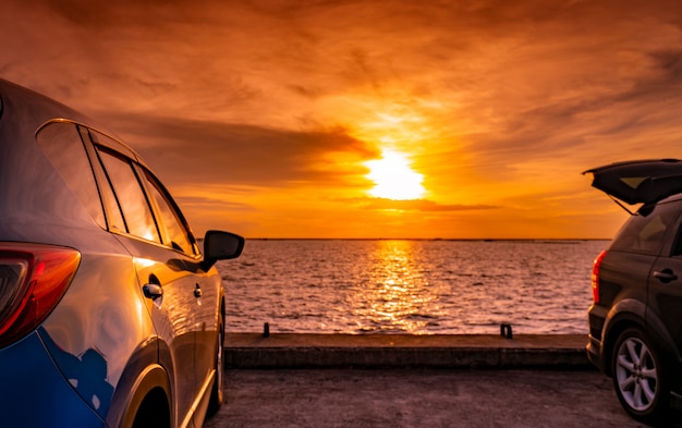 Voiture SUV noir et bleu avec sport et design moderne garée sur une route en béton au bord de la mer au coucher du soleil. Technologie respectueuse de l'environnement. Voyage de voyage en vacances.