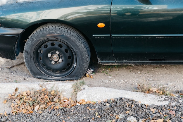 Voiture verte avec une roue crevée en plein air. Pneu crevé endommagé d'une voiture.