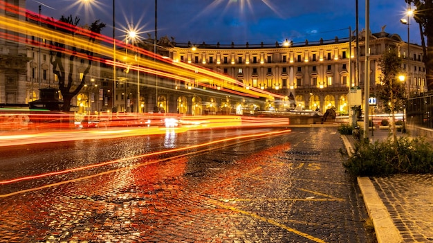 Les voitures allument des sentiers sur la place du soir à Rome après la pluie Routes de circulation nocturne Flou de mouvement