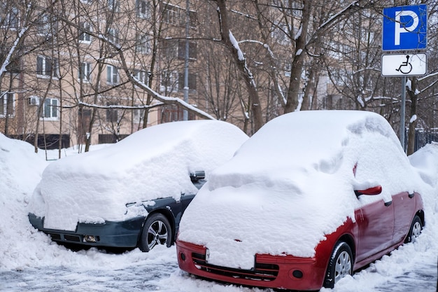 Les voitures enneigées avec une grande couche de neige se tiennent dans un parking