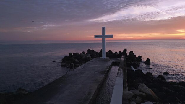 Un vol autour d'une croix chrétienne tôt le matin au lever du soleil La grande croix se trouve au bord d'un brise-lames sur la côte.