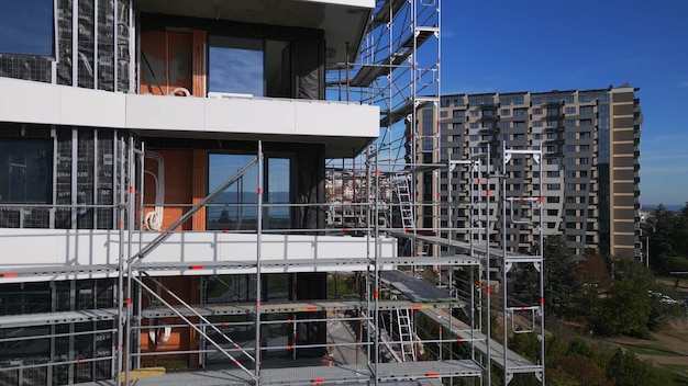 Vol de drone le long de la façade d'un immeuble d'appartements moderne en construction entouré d'échafaudages