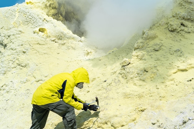 Un volcanologue masculin sur la pente d'un volcan à côté d'une fumerolle de soufre fumante examine un échantillon d'un minéral