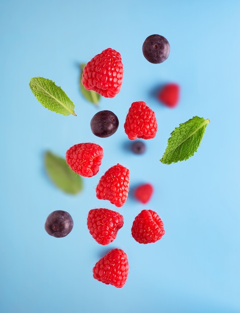 Voler des baies sur une table bleue. Chute de framboises et de menthe