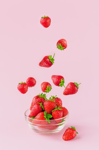 Voler des fraises fraîches dans un bol en verre transparent. Une alimentation saine sur fond rose clair