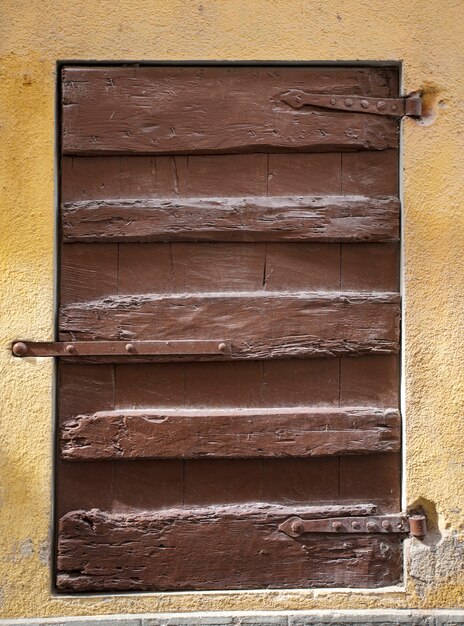 Photo volets de fenêtre en bois brun rustique avec fond de mur en pierre jaune.