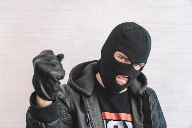 Voleur dans une veste noire Un homme dans une cagoule noire avec une expression maléfique sur son visage Un bandit agressif sur fond blanc Le concept de crime ou de vol