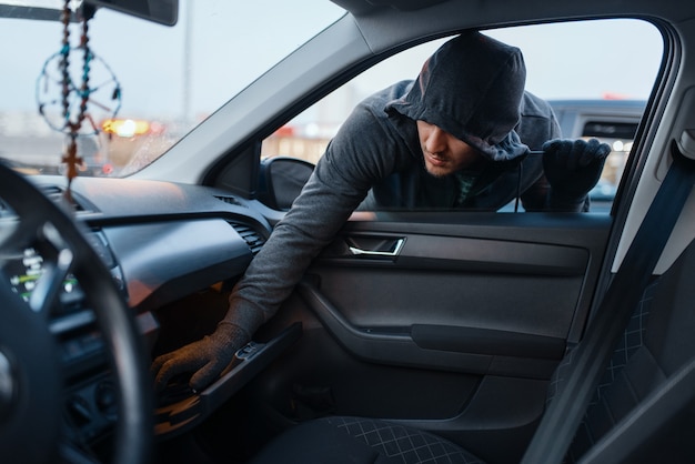 Un voleur de voiture vole le sac à main des femmes, le style de vie criminel, le vol. Véhicule d'ouverture de bandit mâle à capuchon sur le parking. Vol de voiture