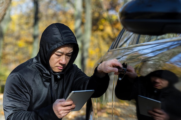 Voleur de voiture voleur bandit mâle asiatique utilise une tablette pour éteindre l'alarme de la voiture