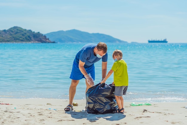 Volontaires masque bleu paradis plage sable lazur mer Père fils ramasser les ordures dans un sac noir Problème ordures déversées poubelle planète pollution protection de l'environnement éducation des enfants naturels