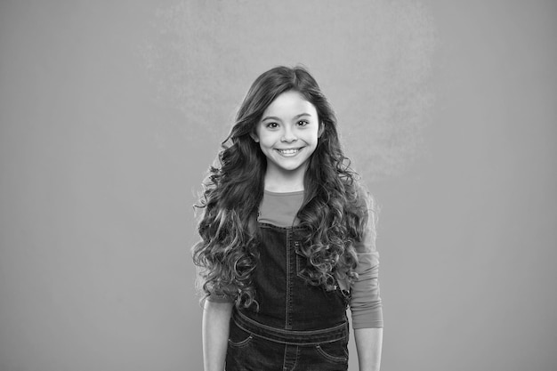 Volume de cheveux extrême Enfant fille cheveux longs et brillants en bonne santé Enfant visage mignon heureux avec une adorable coiffure bouclée debout sur fond bleu Petite fille pousse les cheveux longs Enseignement de saines habitudes de soins capillaires