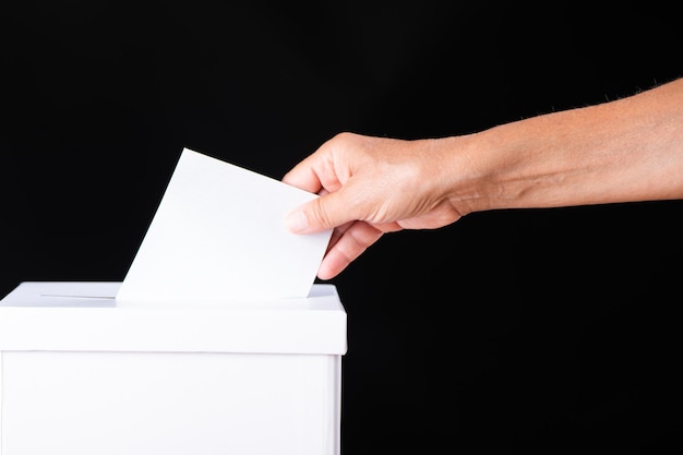 Voter le jour de l'élection Main de femme blanche caucasienne mettant un bulletin de vote blanc dans la boîte