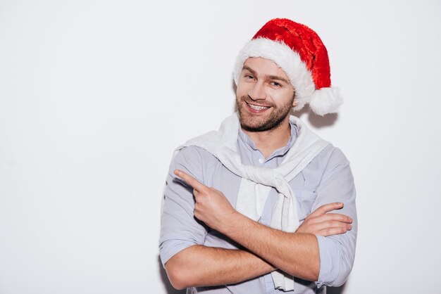 Votre publicité ici ! Beau jeune homme en bonnet de noel pointant vers l'espace de copie et souriant