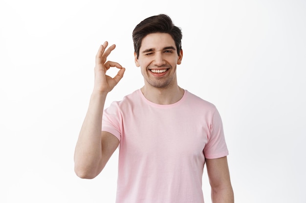 Vous l'avez très bien compris. Un bel homme souriant fait un clin d'œil et montre un signe d'accord, un geste d'accord, loue une bonne chose, complimente votre choix, se tient satisfait sur fond blanc