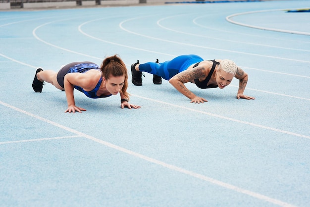 Vous êtes prêt Plan complet de deux jeunes athlètes féminines attirantes faisant des pompes sur la piste