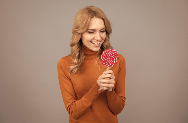 Vous méritez une sucette aujourd'hui Une femme heureuse tient une sucette sur fond gris Malbouffe Mauvaise alimentation Collation sucrée Sweetshop La torsion à laquelle vous ne pouvez pas résister