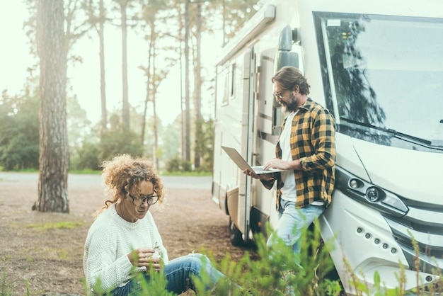 Photo voyage couple adultes homme et femme profitent d'activités de loisirs en plein air à l'extérieur d'un véhicule de camping-car moderne parking dans la forêt voyageur aventurier vanlife style de vie nomade numérique utilisant un ordinateur