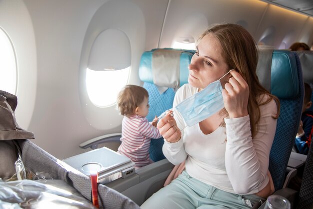 voyage avec un enfant covid19 jeune mère en chaise d'avion met un masque respiratoire médical