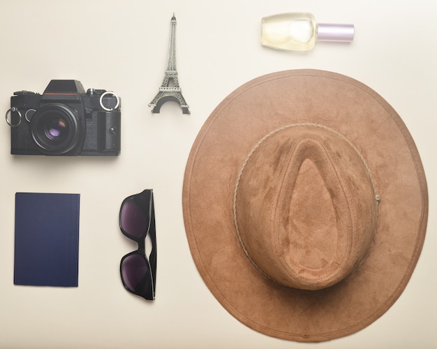 Voyage en France, Paris. Chapeau en feutre, appareil photo argentique, lunettes de soleil, passeport, flacon de parfum, statuette souvenir de la disposition de la Tour Eiffel sur fond de papier pastel.