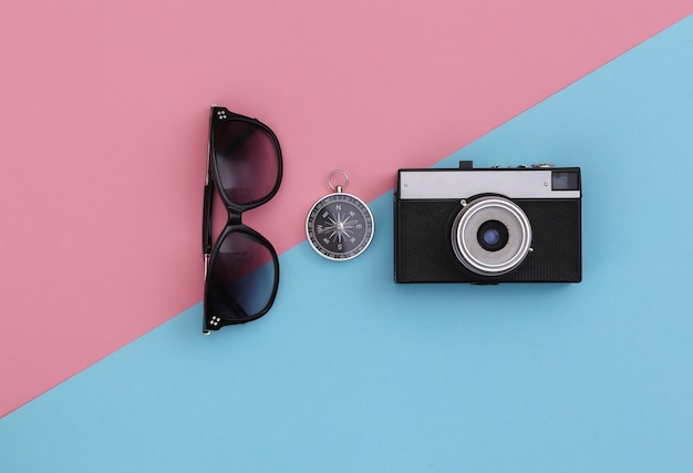 Voyage minimalisme, aventure à plat. Appareil photo, lunettes de soleil et boussole sur fond pastel bleu-rose. Vue de dessus