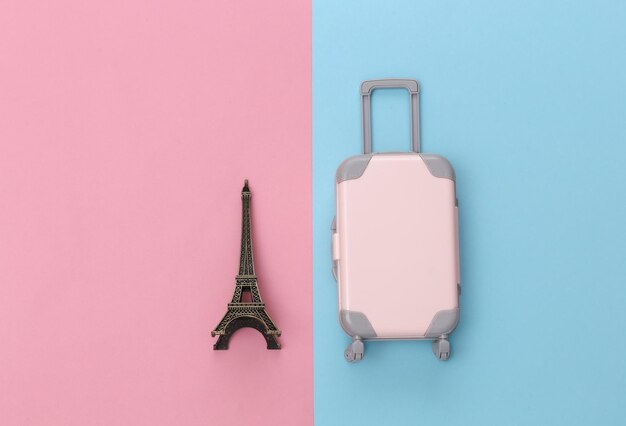 Photo voyage à paris. mini valise de voyage en plastique et statuette de la tour eiffel sur fond rose bleu pastel. vue de dessus. mise à plat