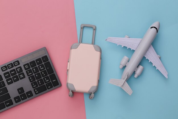 Voyage à plat. Clavier PC et mini bagage de voyage, avion sur bleu rose