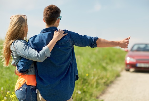 voyage en route, auto-stop, voyage, geste et concept de personnes - couple heureux en auto-stop et arrêt de voiture à la campagne