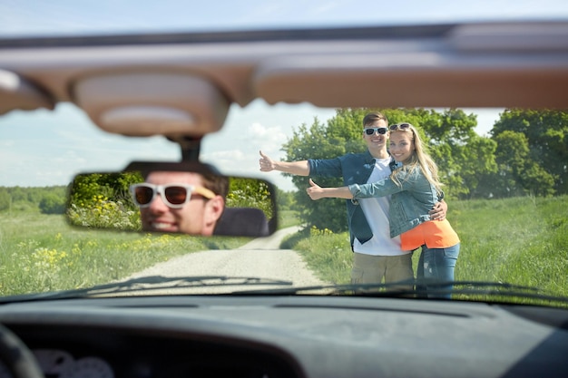 voyage sur la route, auto-stop, voyage, geste et concept de personnes - couple heureux faisant de l'auto-stop et arrêtant la voiture sur la route de campagne