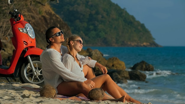 Voyage sur la route en scooter Beau couple sur une moto rouge en vêtements blancs sur la plage de sable