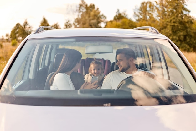 Voyage sur la route de la sécurité des transports familiaux et portrait de personnes d'un homme et d'une femme heureux avec un petit enfant conduisant en voiture voyageant ensemble mère montrant un téléphone portable à l'enfant