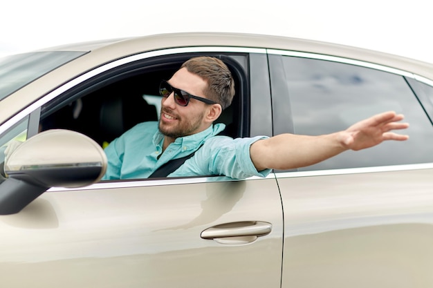 voyage sur la route, transport, voyage et concept de personnes - homme souriant heureux dans des lunettes de soleil conduisant une voiture et agitant la main