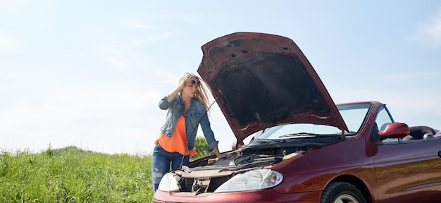 voyage sur la route, transport, voyage et concept de personnes - jeune femme avec capot ouvert de voiture cassée à la campagne