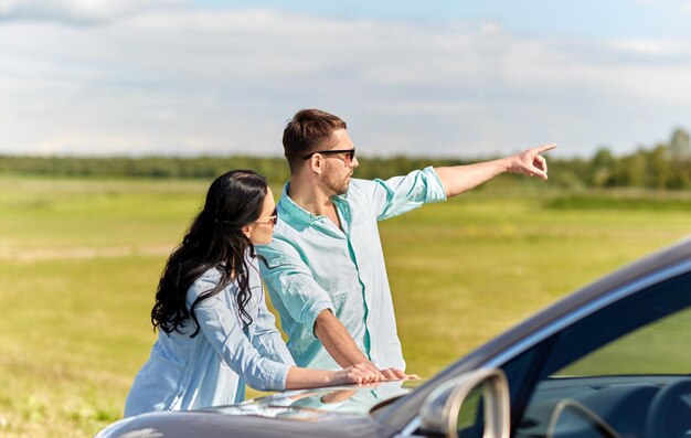 voyage sur la route, voyage, tourisme, concept de famille et de personnes - homme et femme heureux recherchant l'emplacement et pointant le doigt vers la voiture à l'extérieur