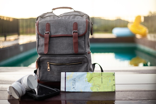 Voyage avec sac à dos avec casque carte appareil photo écouteur et téléphone intelligent sur la piscine dans la villa avec piscine