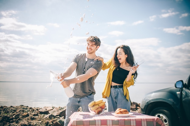 Voyage, tourisme - Pique-nique au bord de l'eau. Couple à l'aventure. Concept de voyage en voiture. Homme et femme boivent du champagne.