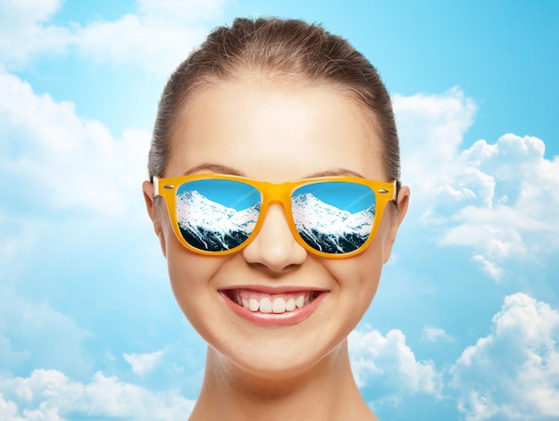 voyage, tourisme, station d'hiver et concept de personnes - visage heureux d'une adolescente en lunettes de soleil avec reflet de montagnes sur fond bleu ciel et nuages