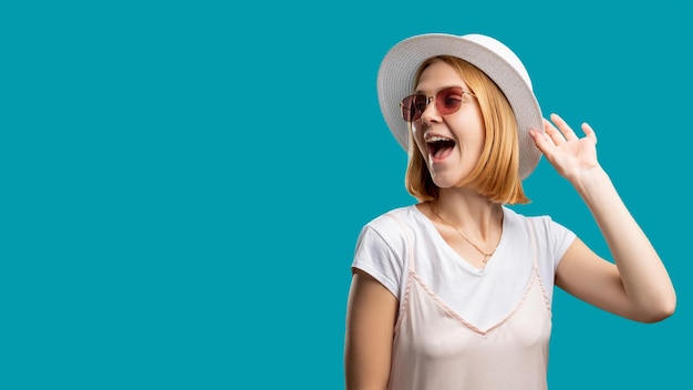 Voyage de vacances Tenue d'été Femme heureuse en blanc et lunettes de soleil touchant le chapeau gitan isolé sur l'espace de copie bleu Agence de voyage Accessoires de protection solaire