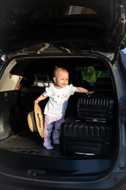 Voyage en voiture avec un enfant Coffre ouvert de la voiture Valises sur la route Bébé avec un chapeau de voyageur